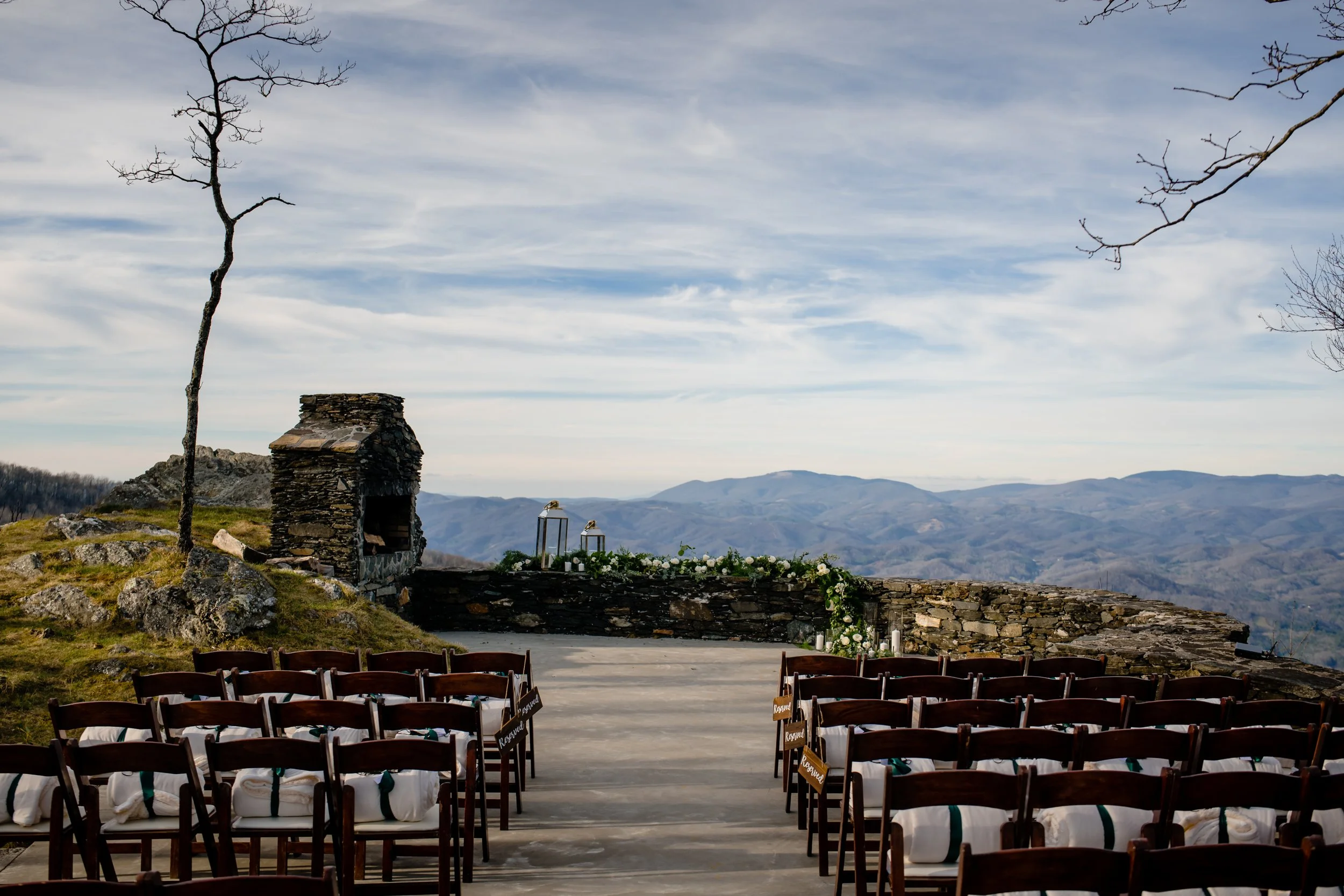 Outdoor wedding ceremony site with rows of chairs facing a stone wall and mountain views.