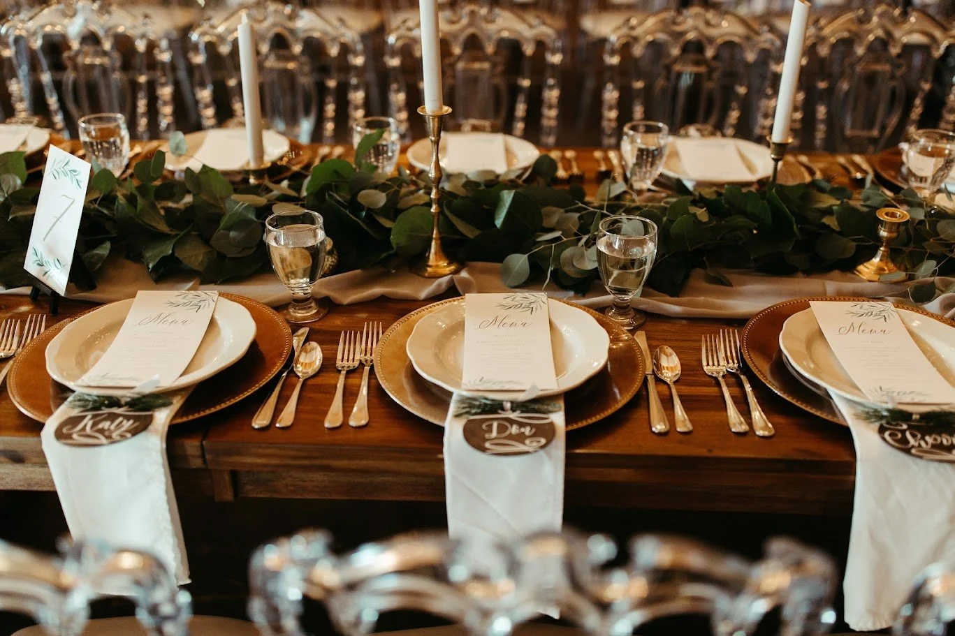 Rustic wedding reception table with place settings, greenery, candles, and floral centerpieces.
