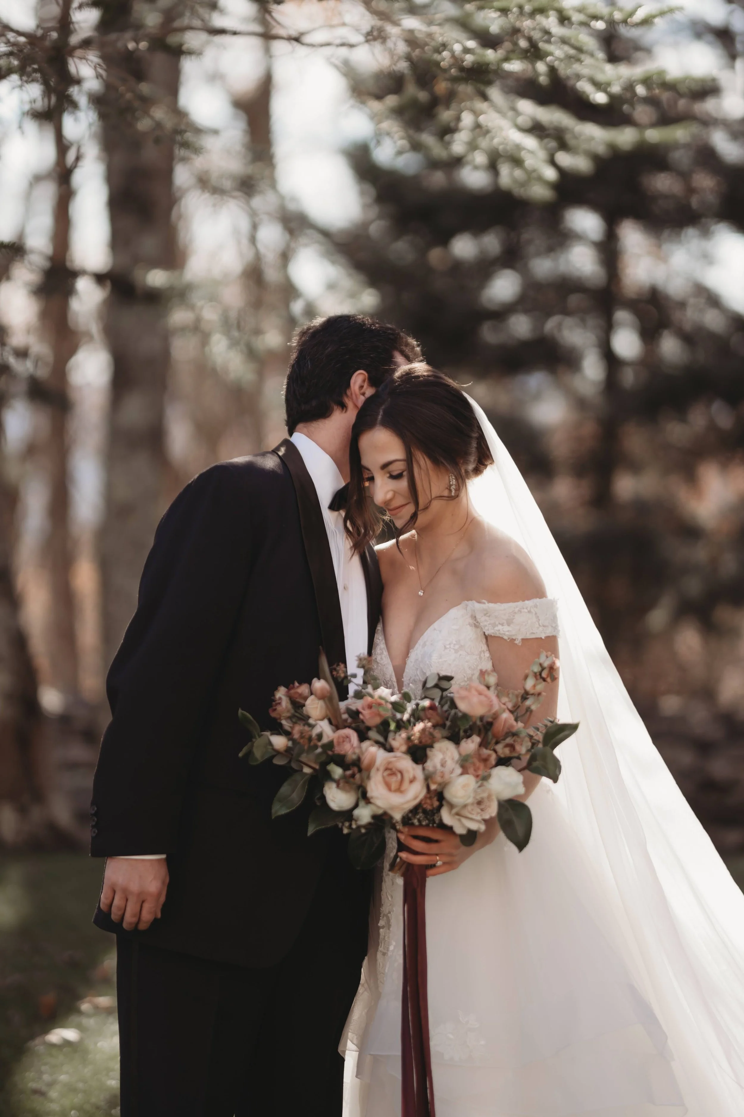 Groom kissing the bride’s forehead during portraits as she holds her bouquet and veil.