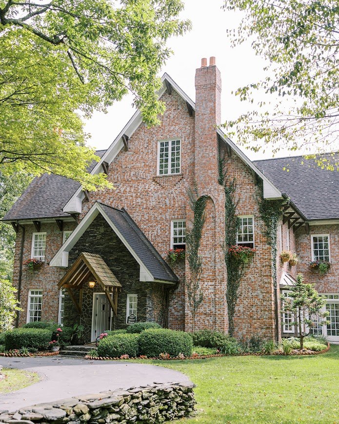 Brick manor wedding venue with steep gables, ivy-covered chimney, and a landscaped front lawn.