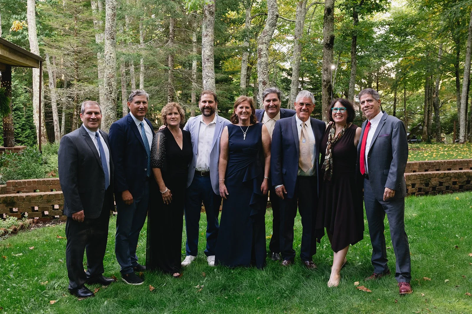 Corporate retreat group posing for a formal portrait on a wooded lawn surrounded by trees and mountain greenery.