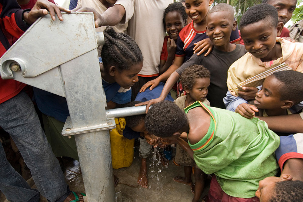 community members drinking from new water tap, charity: water