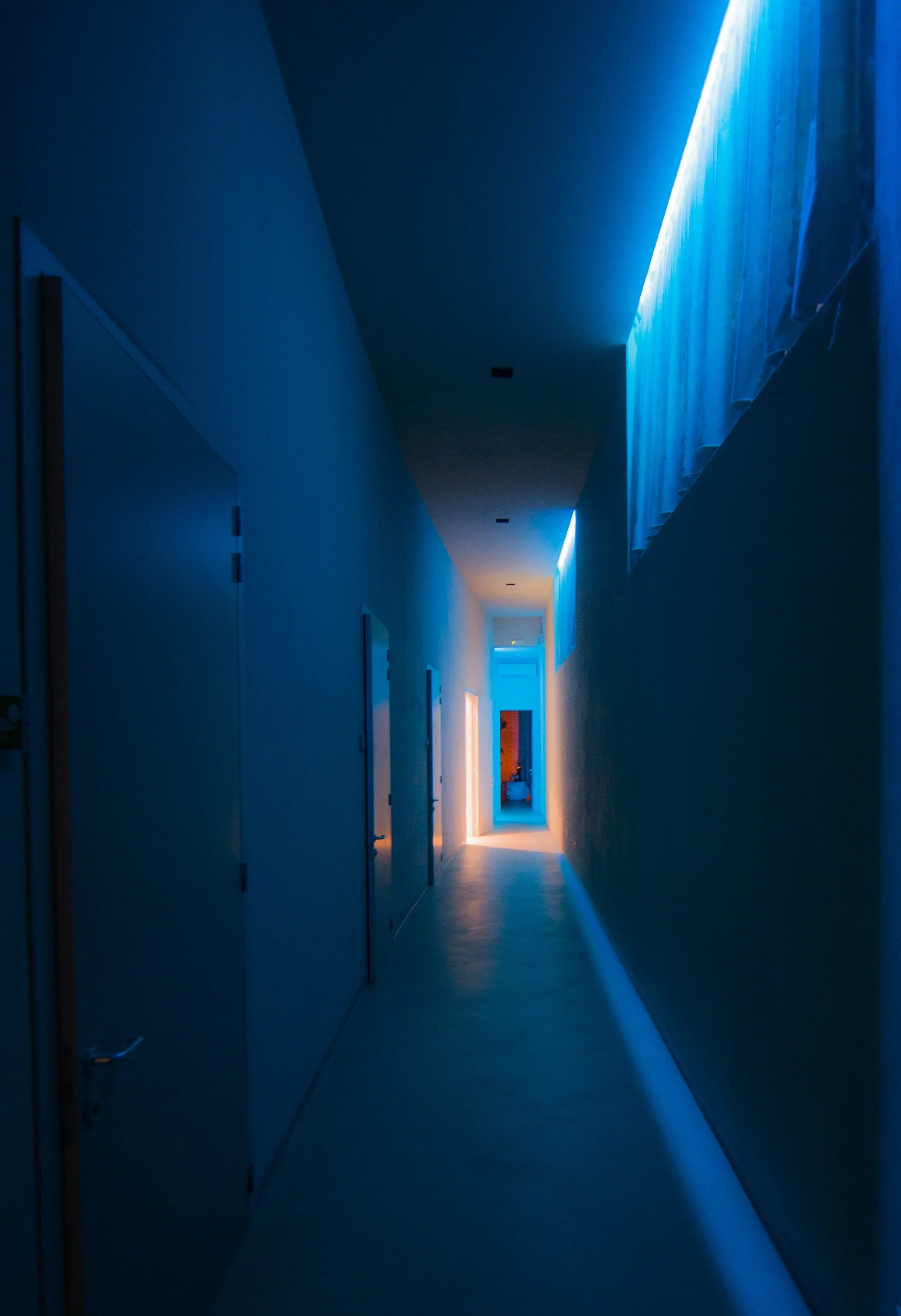 Corridoio con luci di colore blu e arancione, pareti bianche e porte lungo i lati.