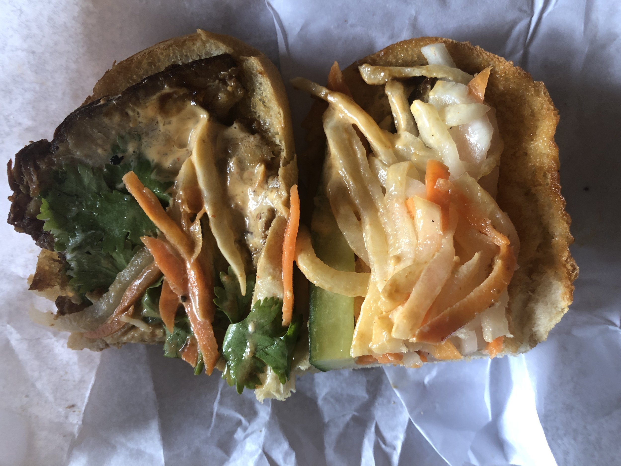In depth look at a mostly eaten pork belly banh mi, meat on left, veggies mainly on right