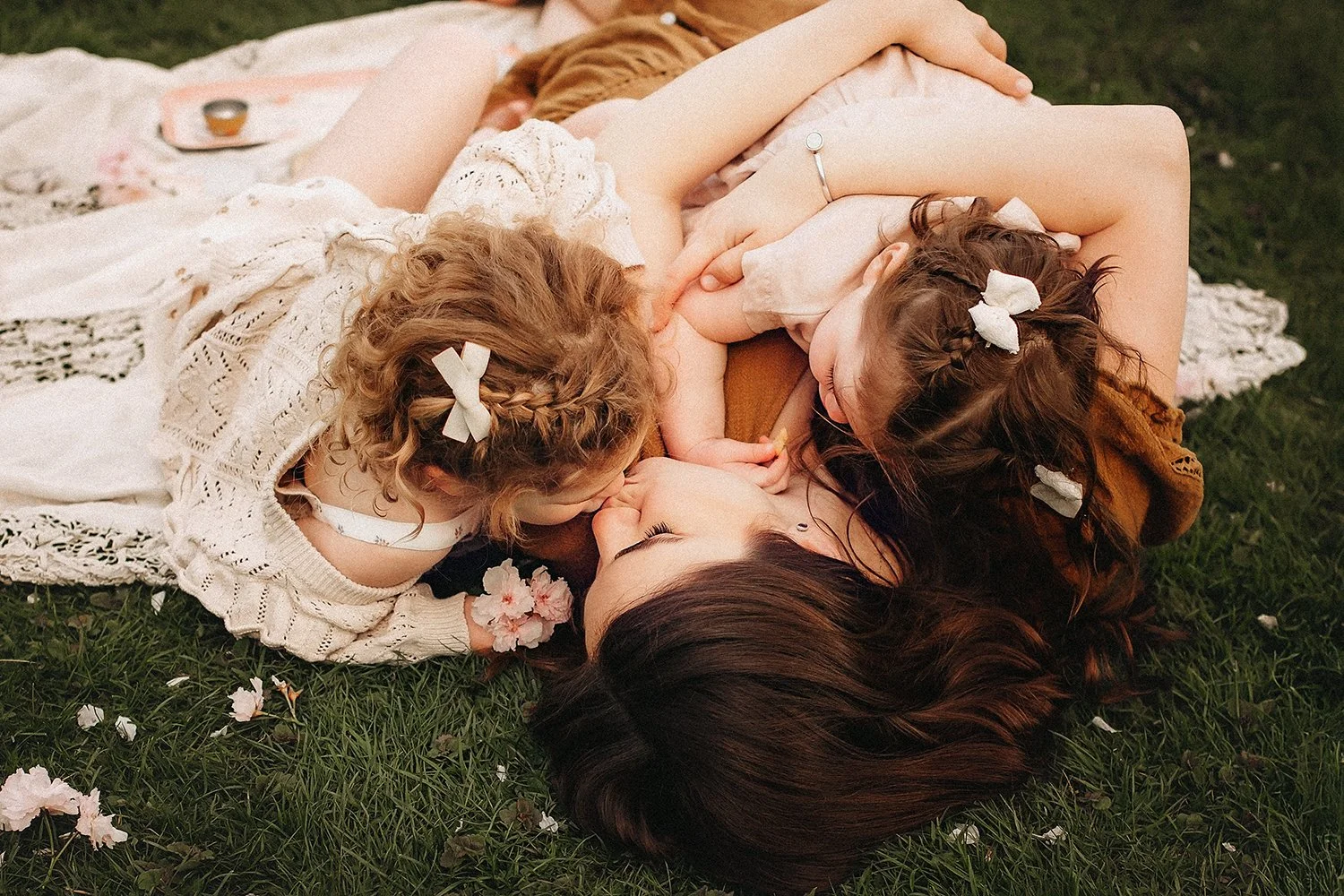 Mom and two daughters enjoying playful moment in cherry blossom field, lifestyle family photos in New Jersey