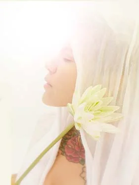 A rose tattooed woman praying holding a long stemmed white lotus flower