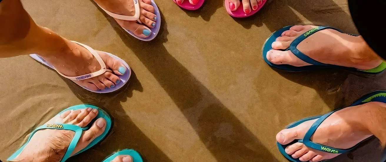 Group of people standing on the beach wearing flip-flops in various colors and sizes.