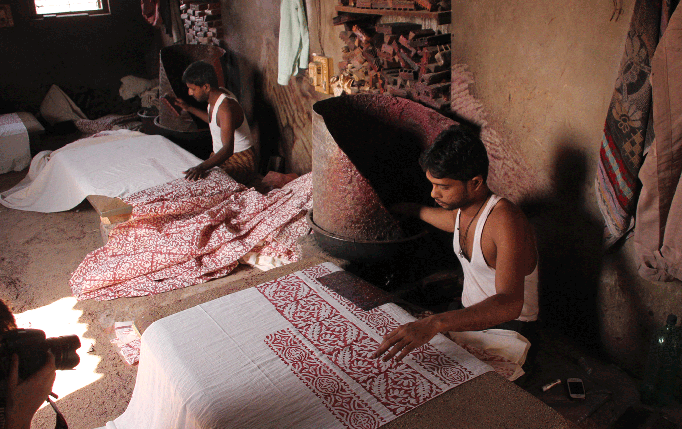 Batik printing is often done on low tables, on a surface of sand. The printer sits near the burner for easy access to the wax
