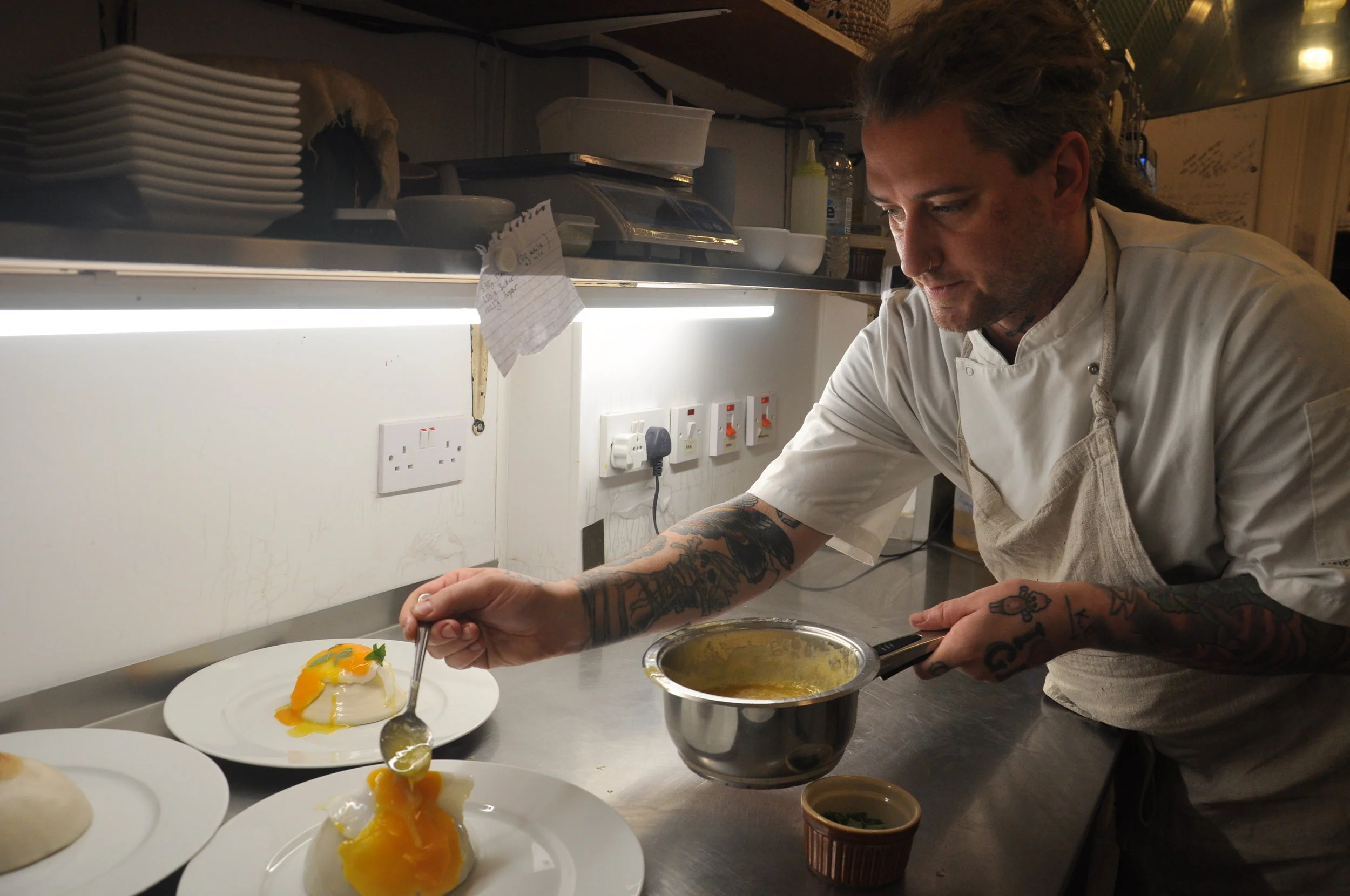 Brandon Baltzley pours butter sauce over a fried duck egg balanced on a ceramic boob