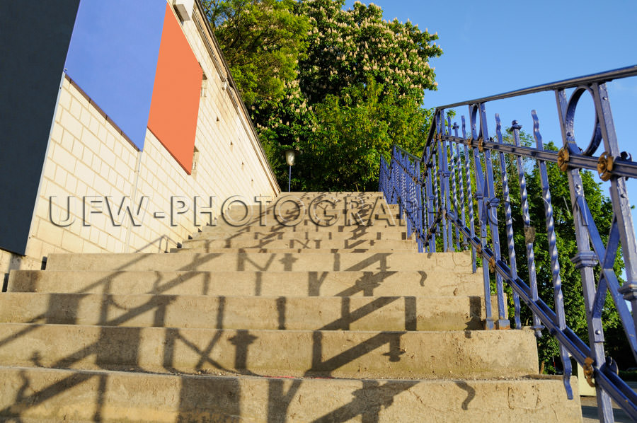 Ascending stone staircase, blue banister, clear sky, green chest