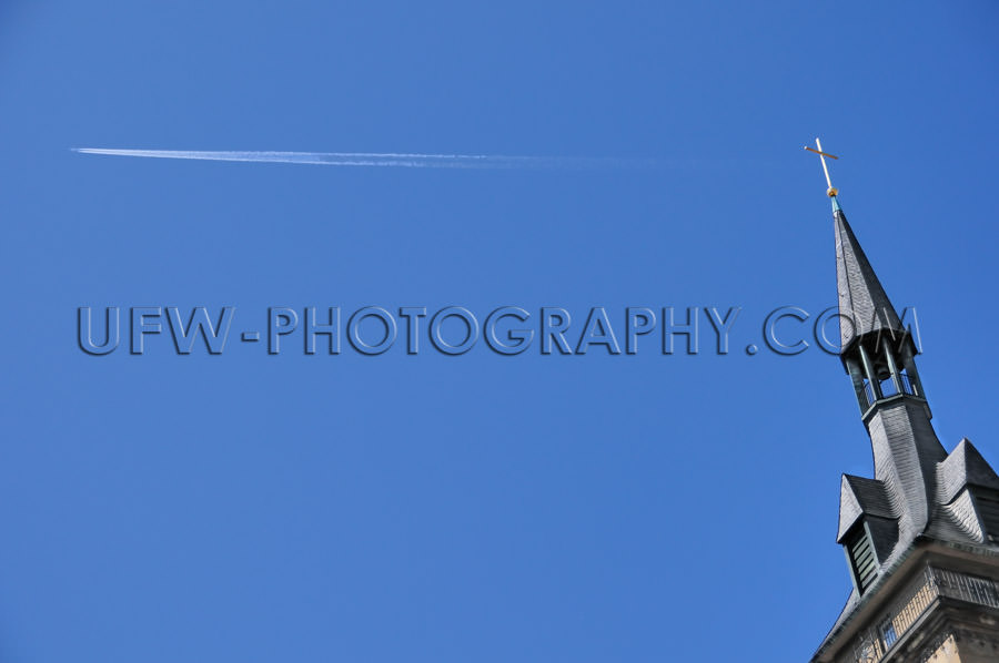 Church steeple, golden cross, jet stream against deep blue sky -