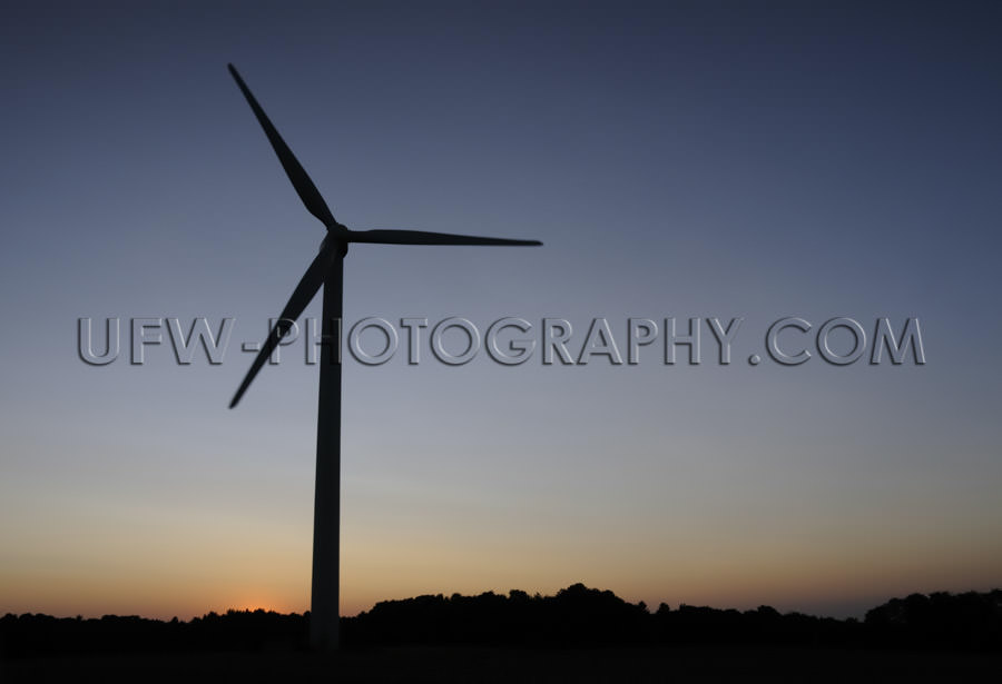 Black wind turbine silhouette, dark blue and orange night sky - 