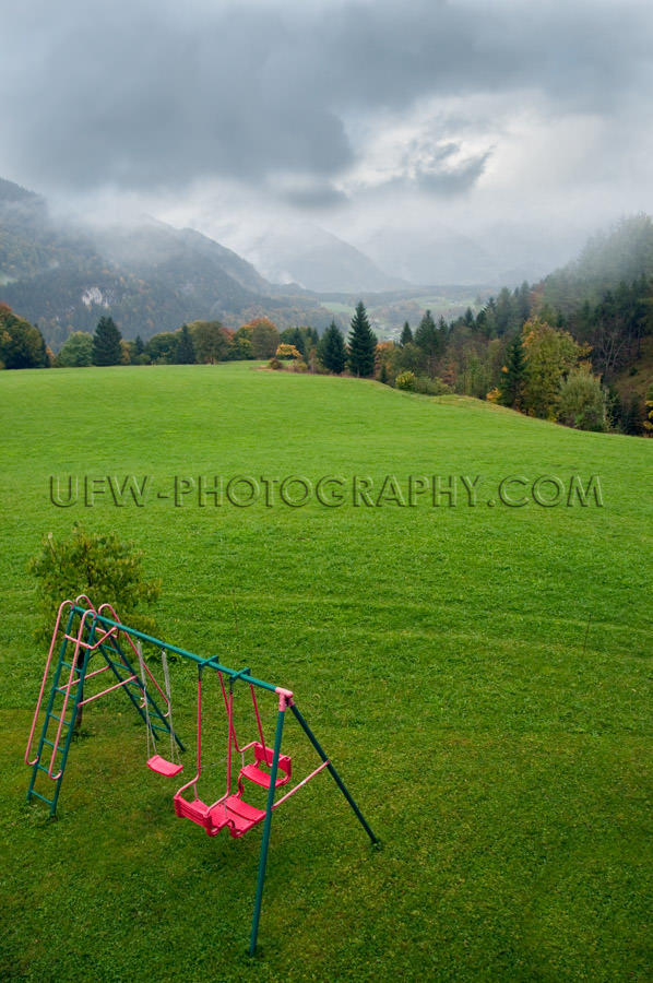 Green mountain pasture dramatic sky playground swing red Stock I