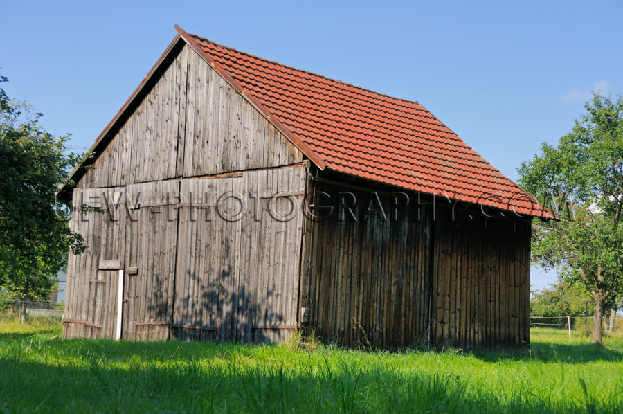 Wooden barn under blue sky with meadow and trees Stock Image