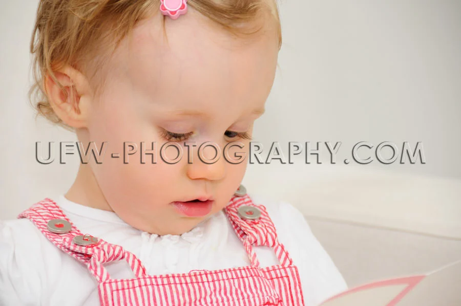 Cute little toddler girl reading card looking down sofa Stock Im