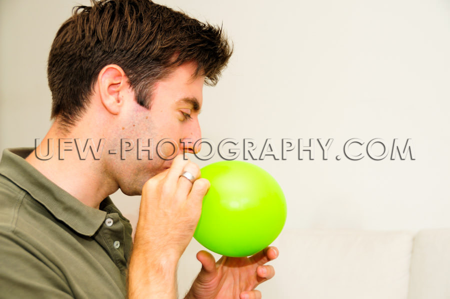 Dad blowing green balloon inflating close-up indoors casual Stoc