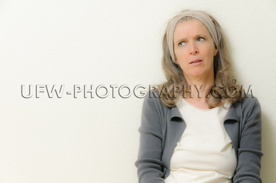 Mature woman pondering leaning wall head-wrap looking up Stock I