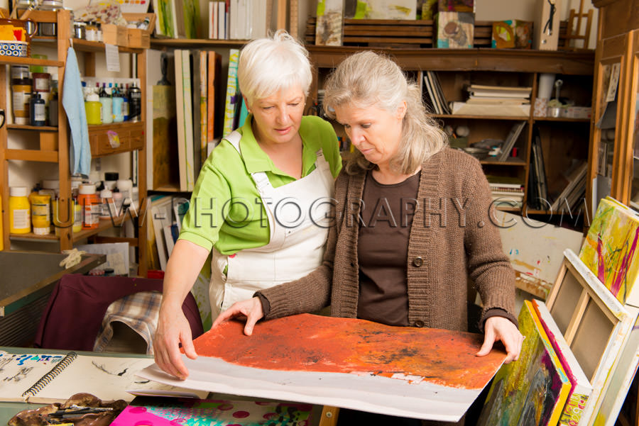 Senior female artist talking to woman showing painting Stock Ima