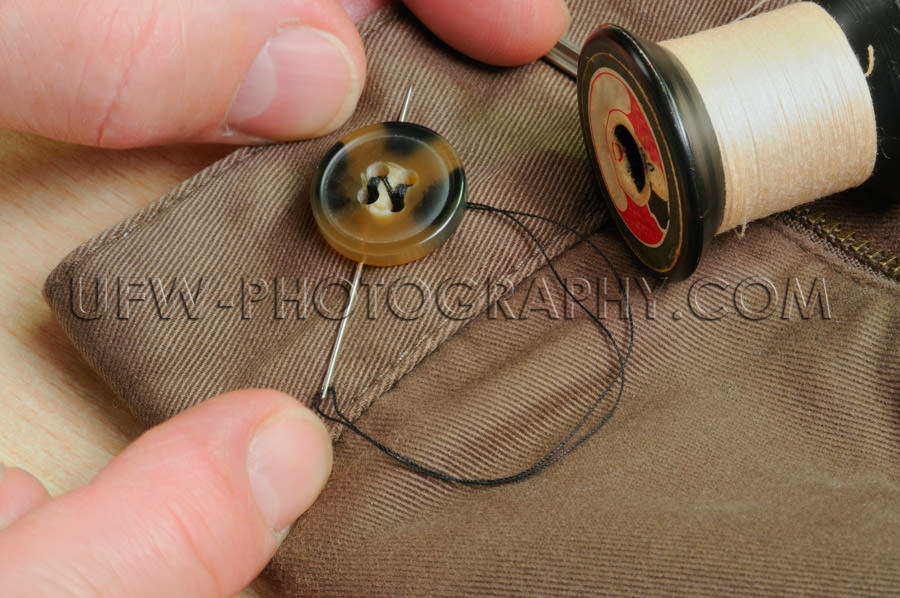 Sewing on a trouser button, macro of household chores - Stock Im