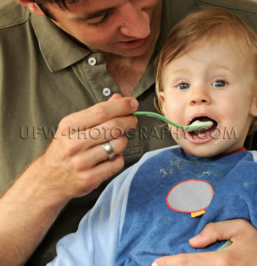 Young father caring feeding one-year-old eating child spoon mout