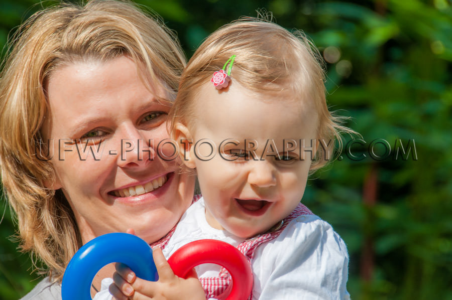 Young mother holding toddler girl happy laughing playful garden 