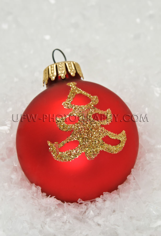 Red xmas bauble with golden tree icon, lying in snow - Stock Ima