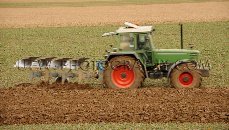 Cute little green tractor with red wheels, plowing in spring - S