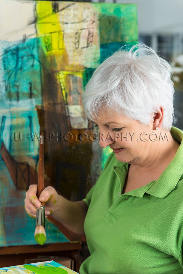 Ältere Frau trägt ein grünes T-Shirt und malt in Künstlerate