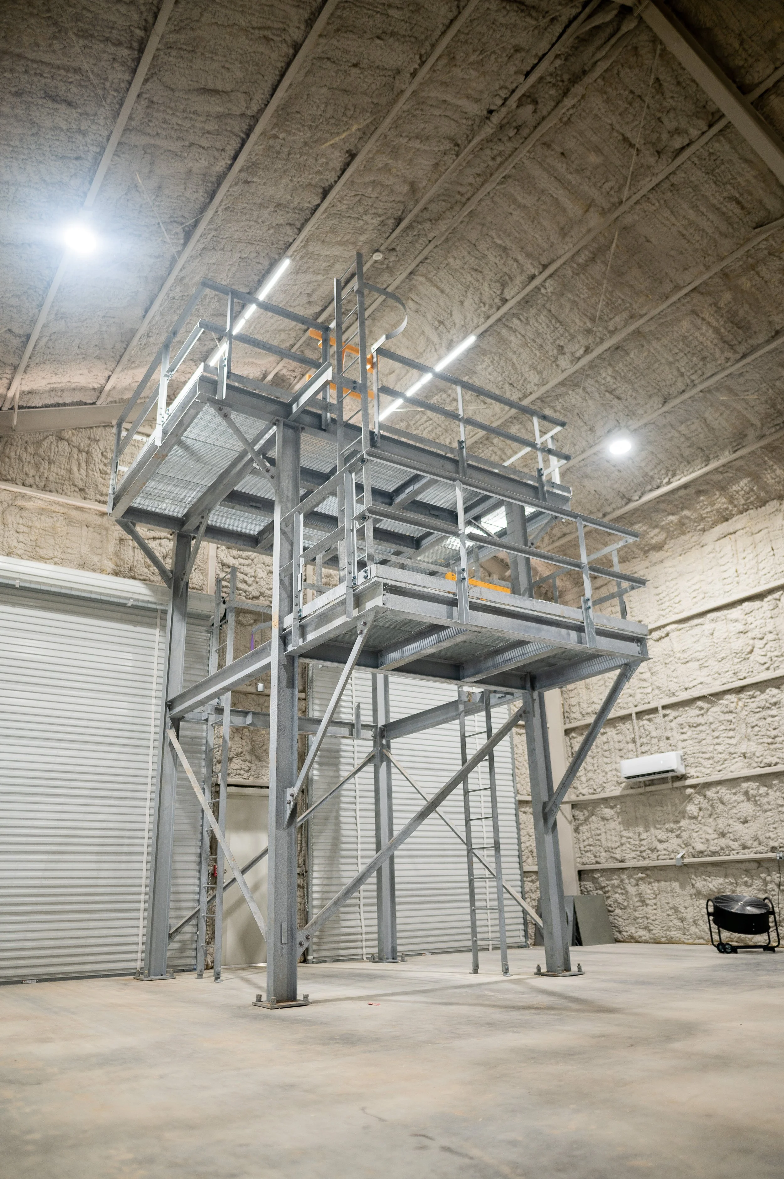 Steel scaffolding structure inside an industrial warehouse with insulated walls and overhead lighting.