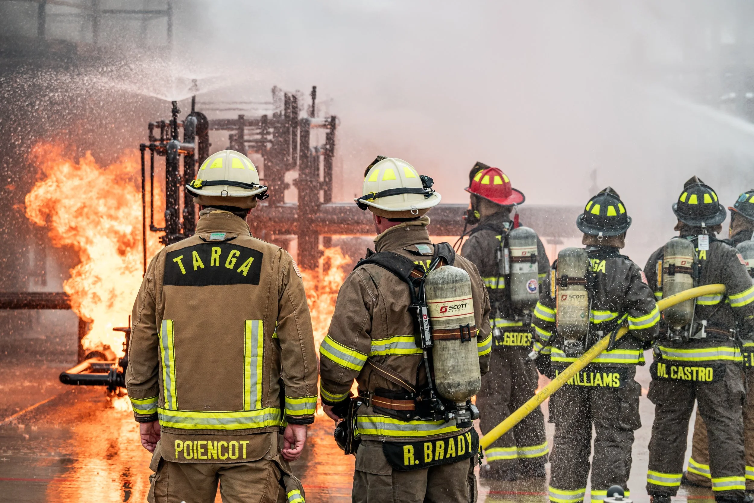 Firefighters in protective gear battling a fire at an industrial site, with flames and smoke in the background.
