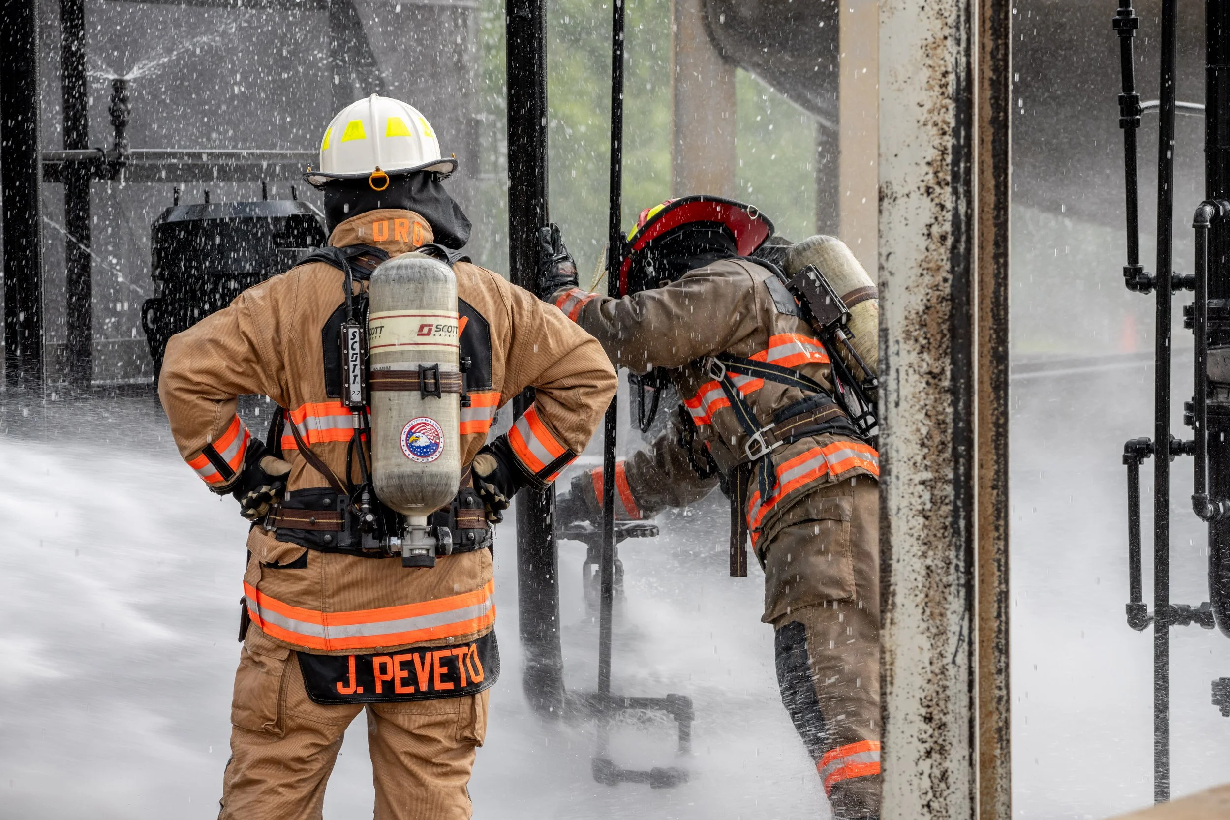 Two firefighters in full gear working during a fire rescue, with water spraying around them.