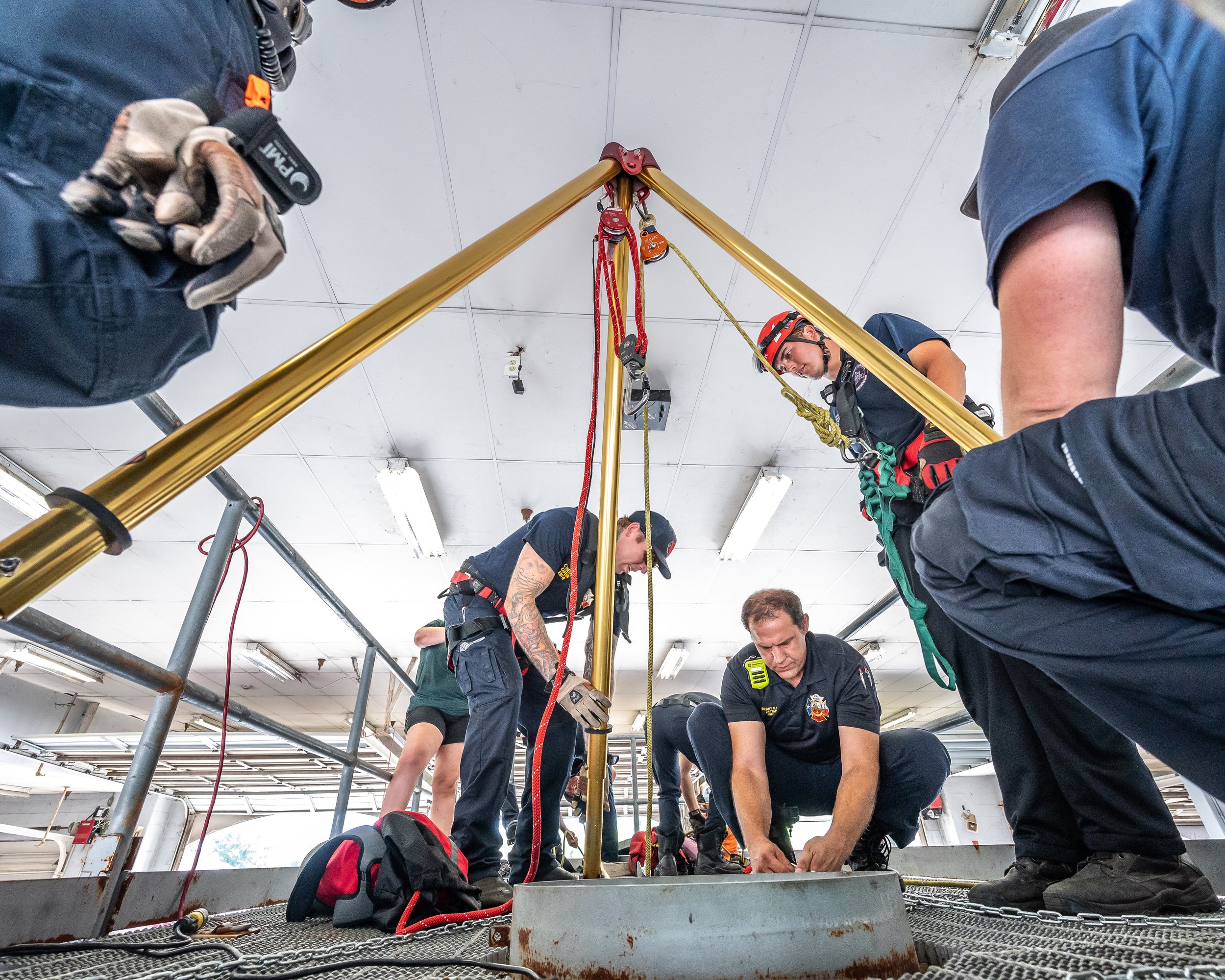 Firefighters working inside a building, preparing equipment and securing a tripod with climbing or rescue gear.