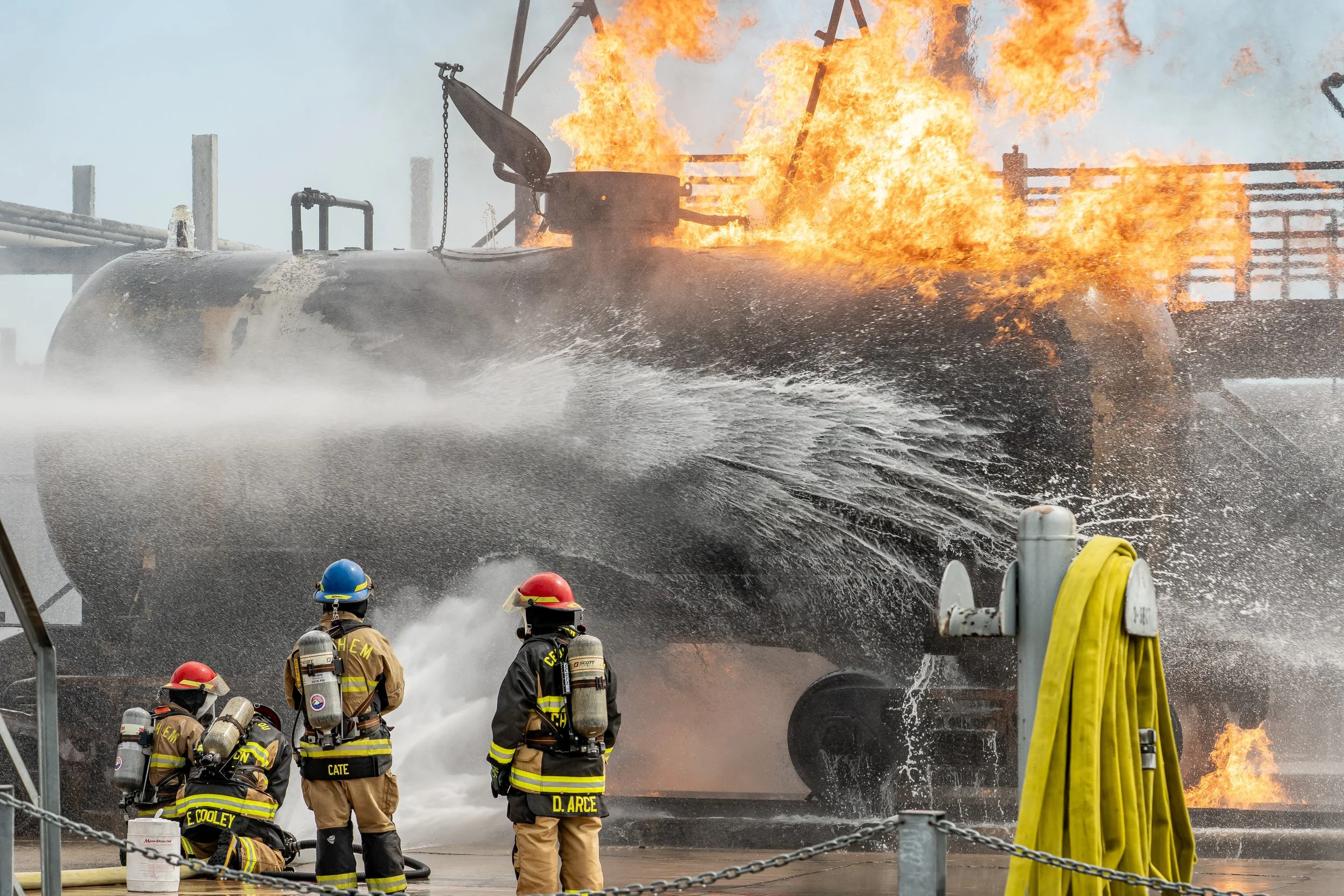 Firefighters in protective gear battling a large fire on a boat or ship, with flames and smoke coming from the vessel.