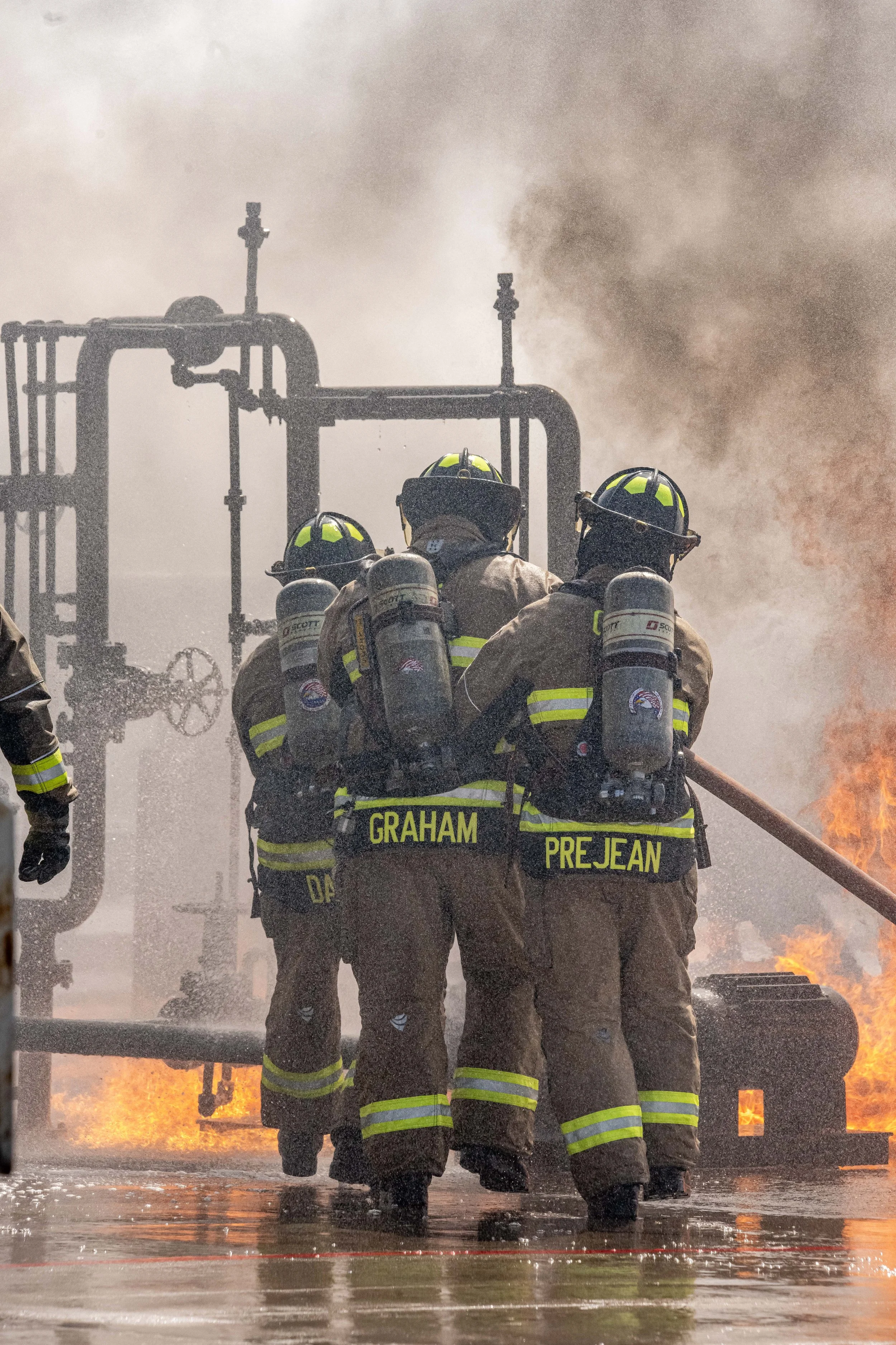 Firefighters working to extinguish a fire on an industrial site, with flames and smoke in the background.