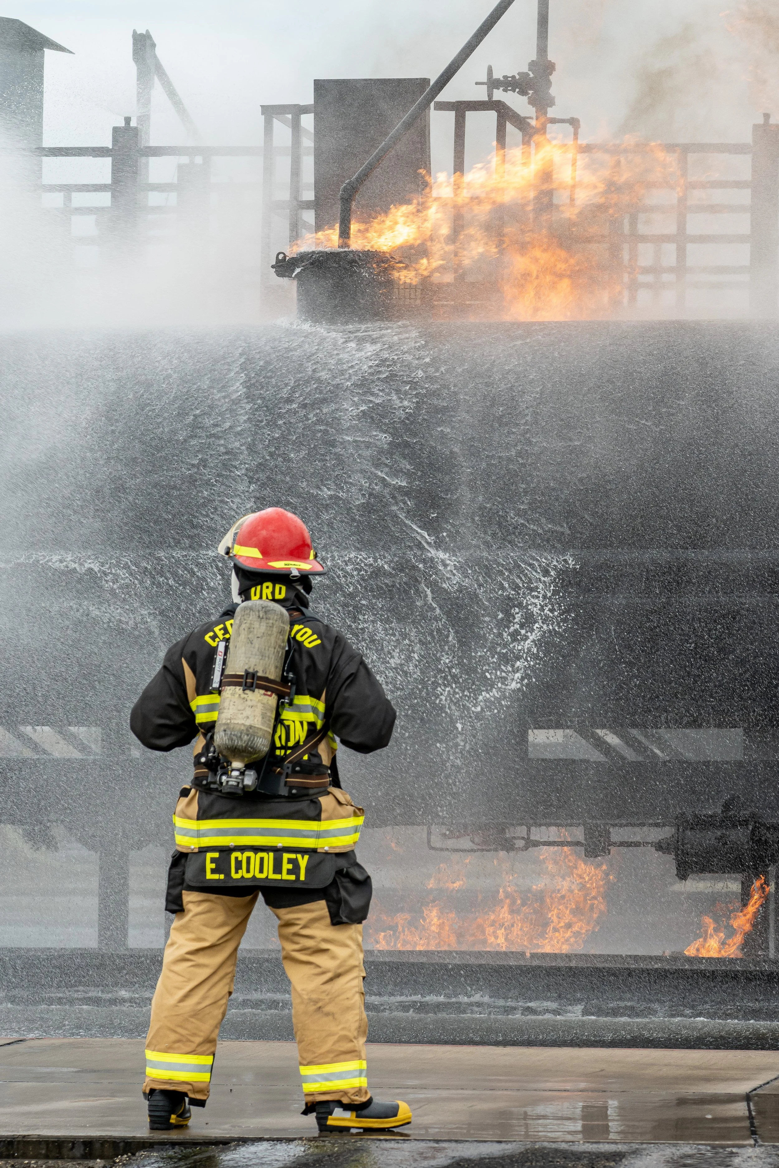 Firefighter in uniform stands facing a building with flames and smoke coming from it during a fire.