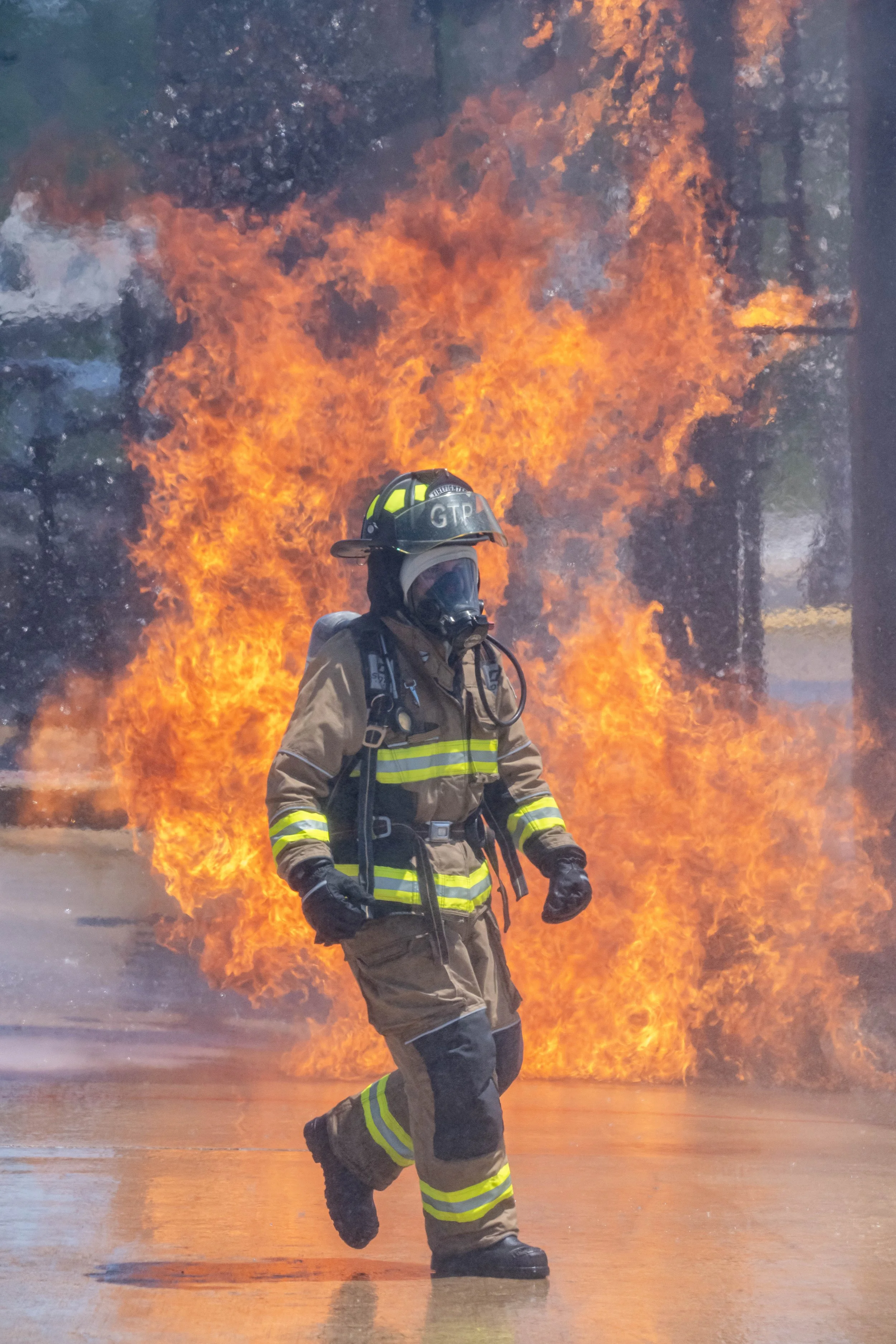 Firefighter in full gear running away from a large fire with flames and smoke.