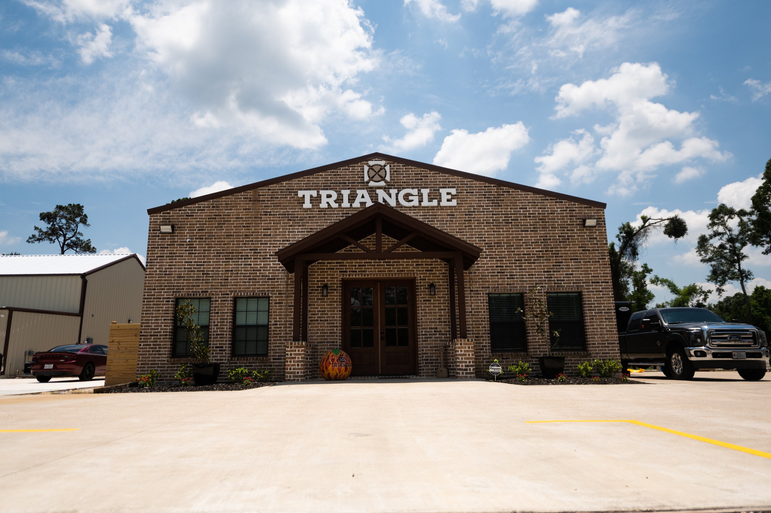 A brick building with the word "TRIANGLE" on it, with a small porch and a pumpkin decoration at the front entrance, under a partly cloudy sky.