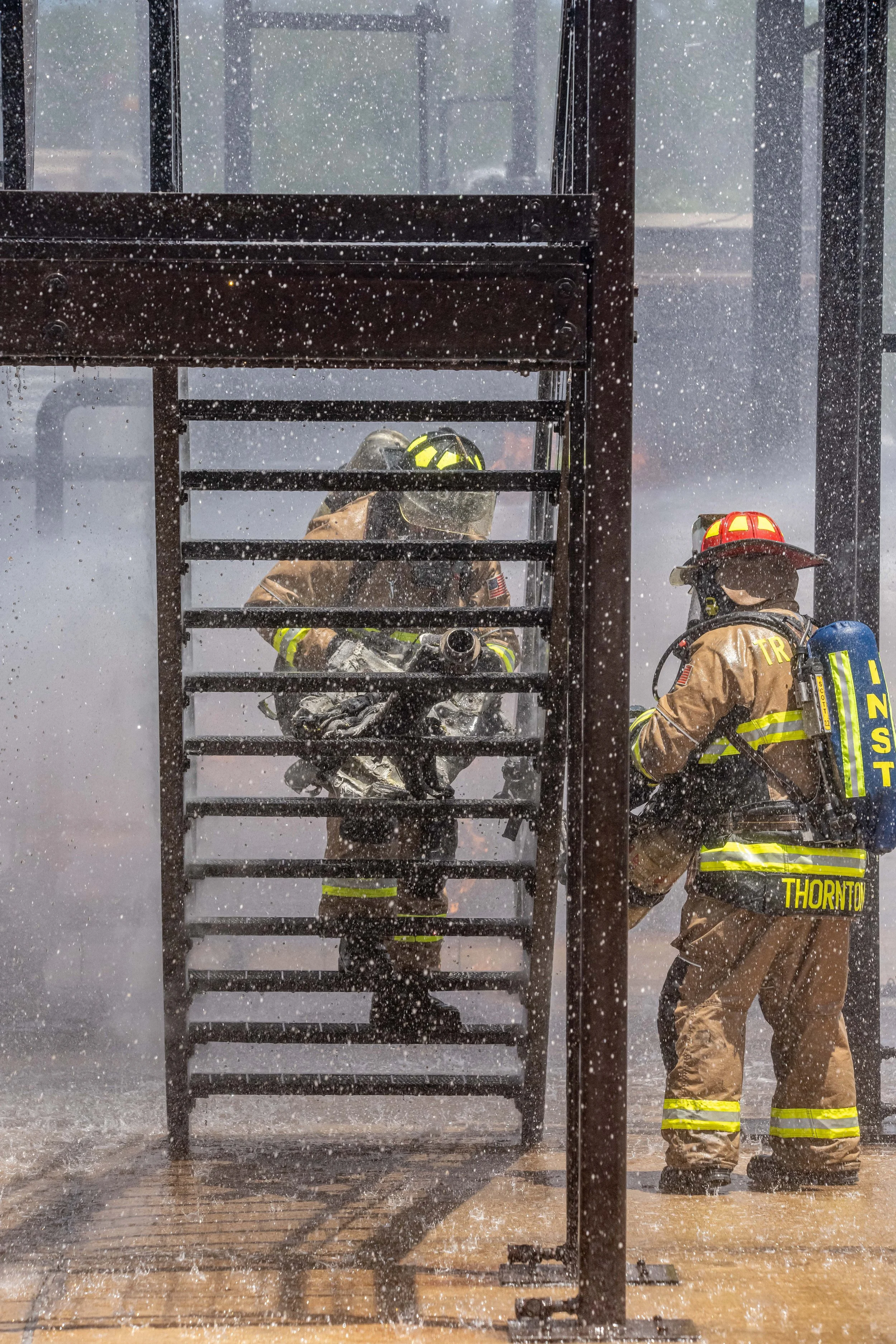 Firefighters in full gear battling a blaze in a structure, with water and smoke visible.