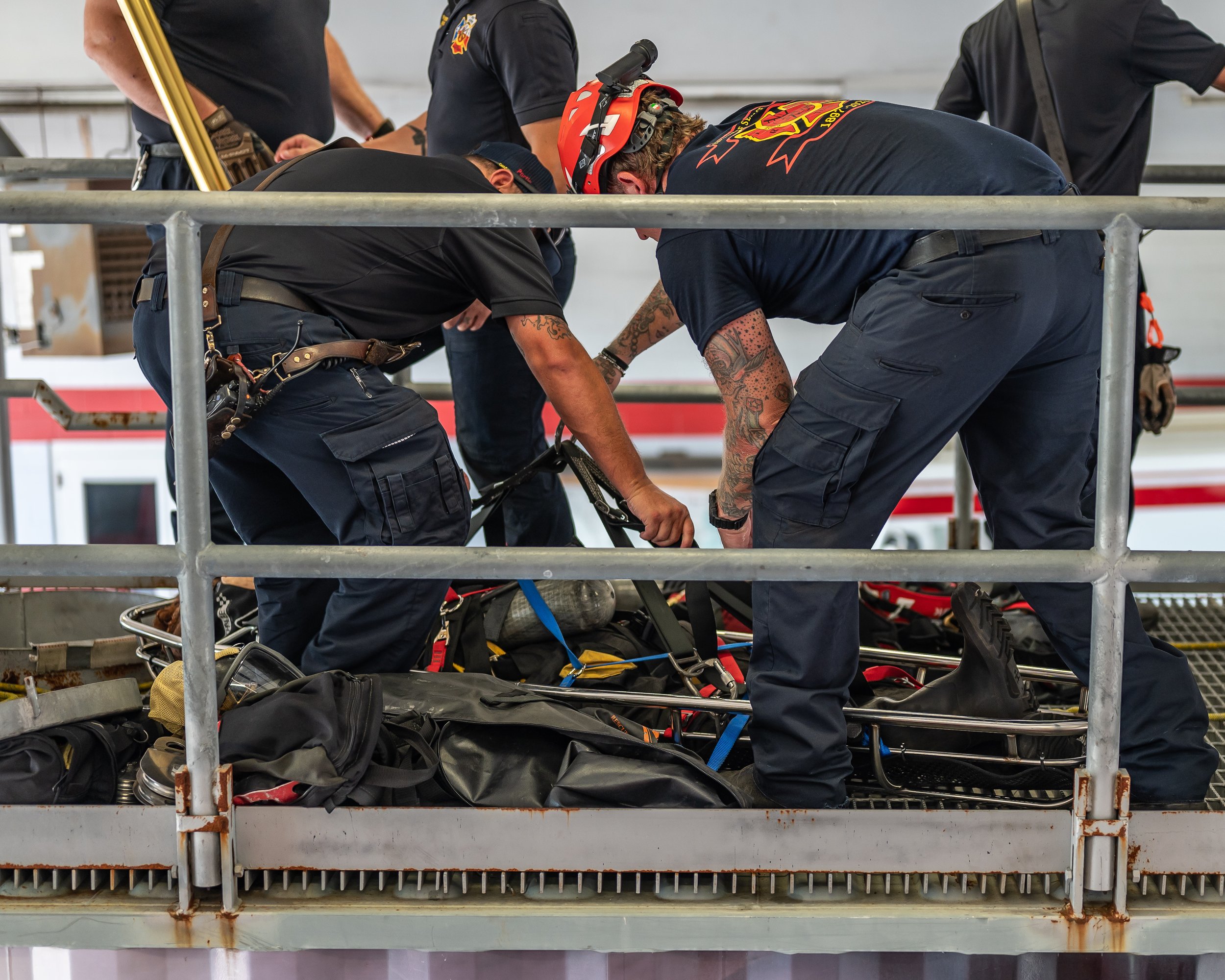 Firefighters are working together to rescue a person from an elevated platform, using a stretcher and safety gear.