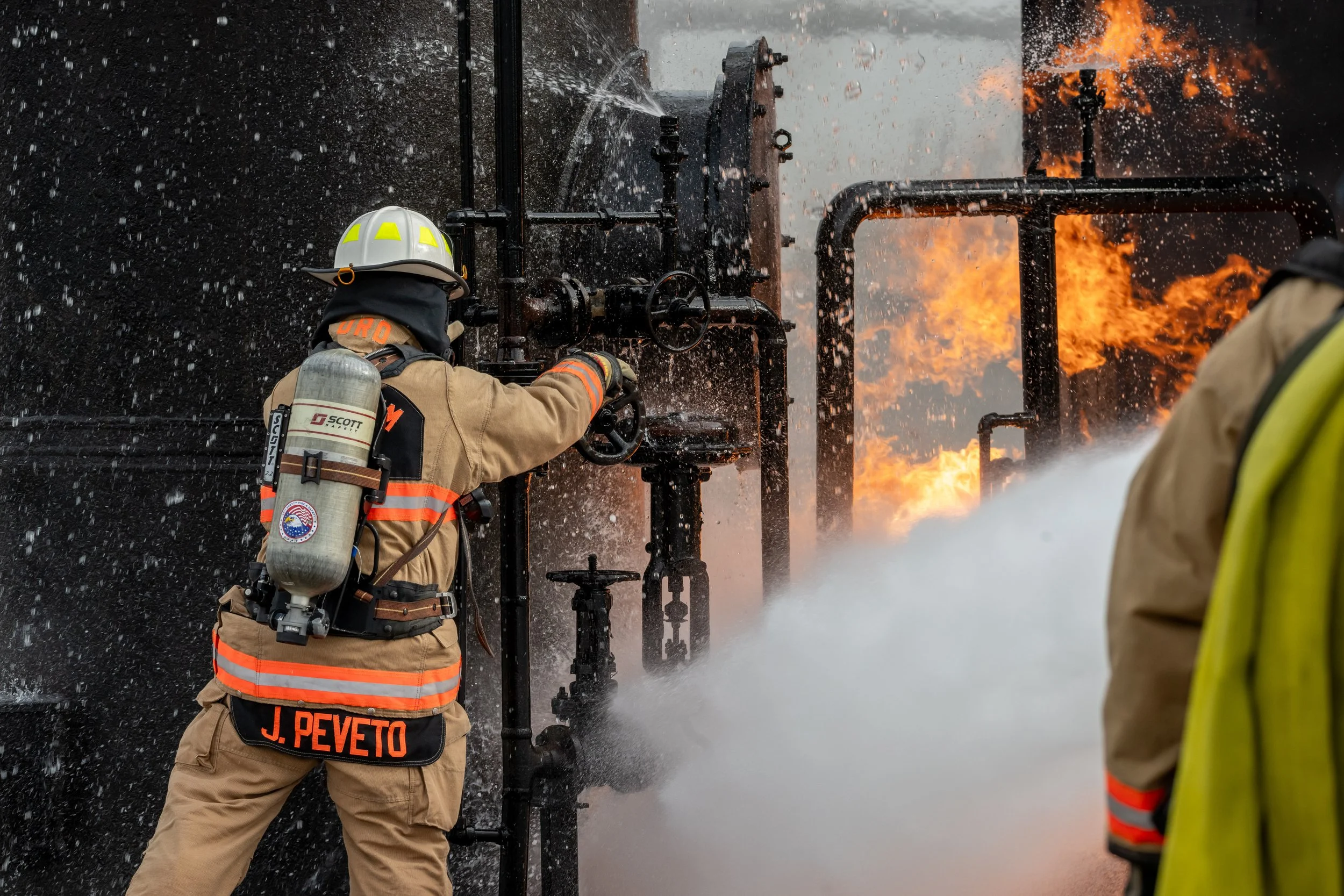Firefighters in protective gear fighting a blaze on a large industrial pipe, with flames and smoke