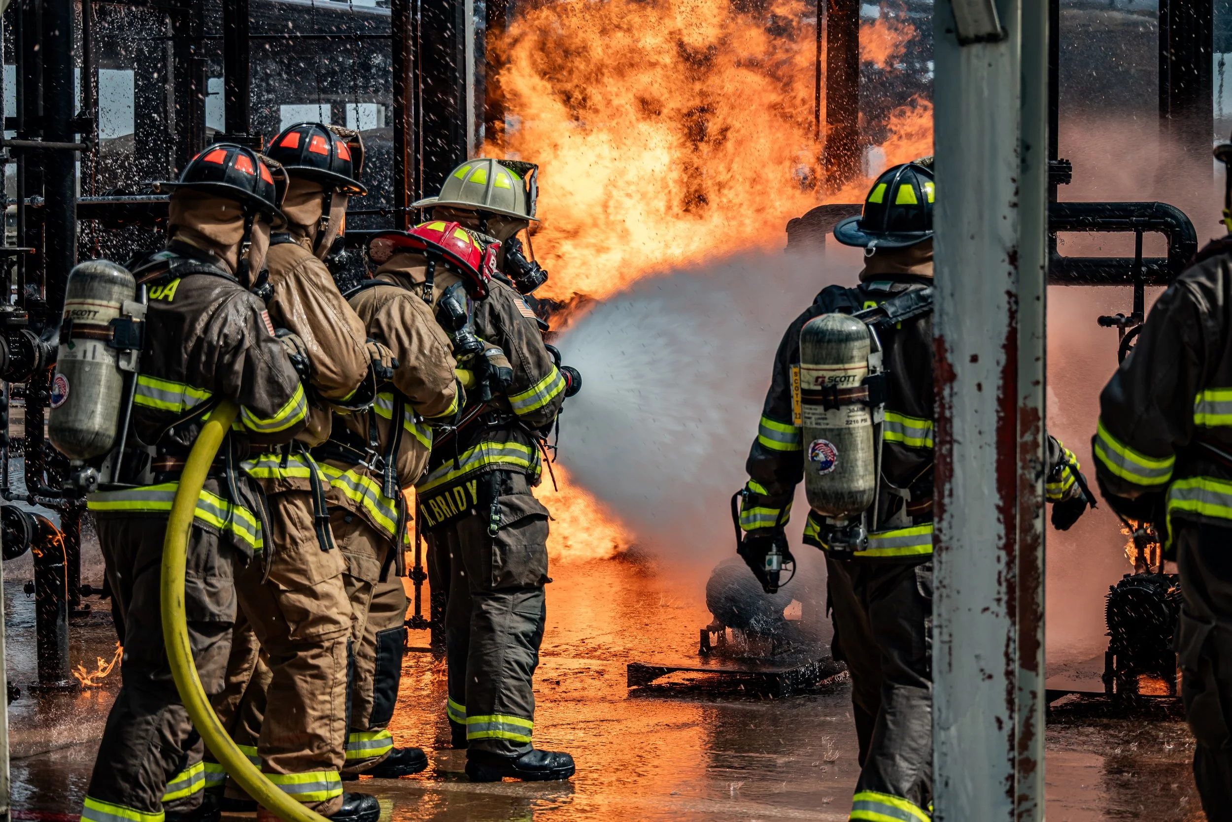 Firefighters in gear battling a fire with flames and smoke in an industrial setting.