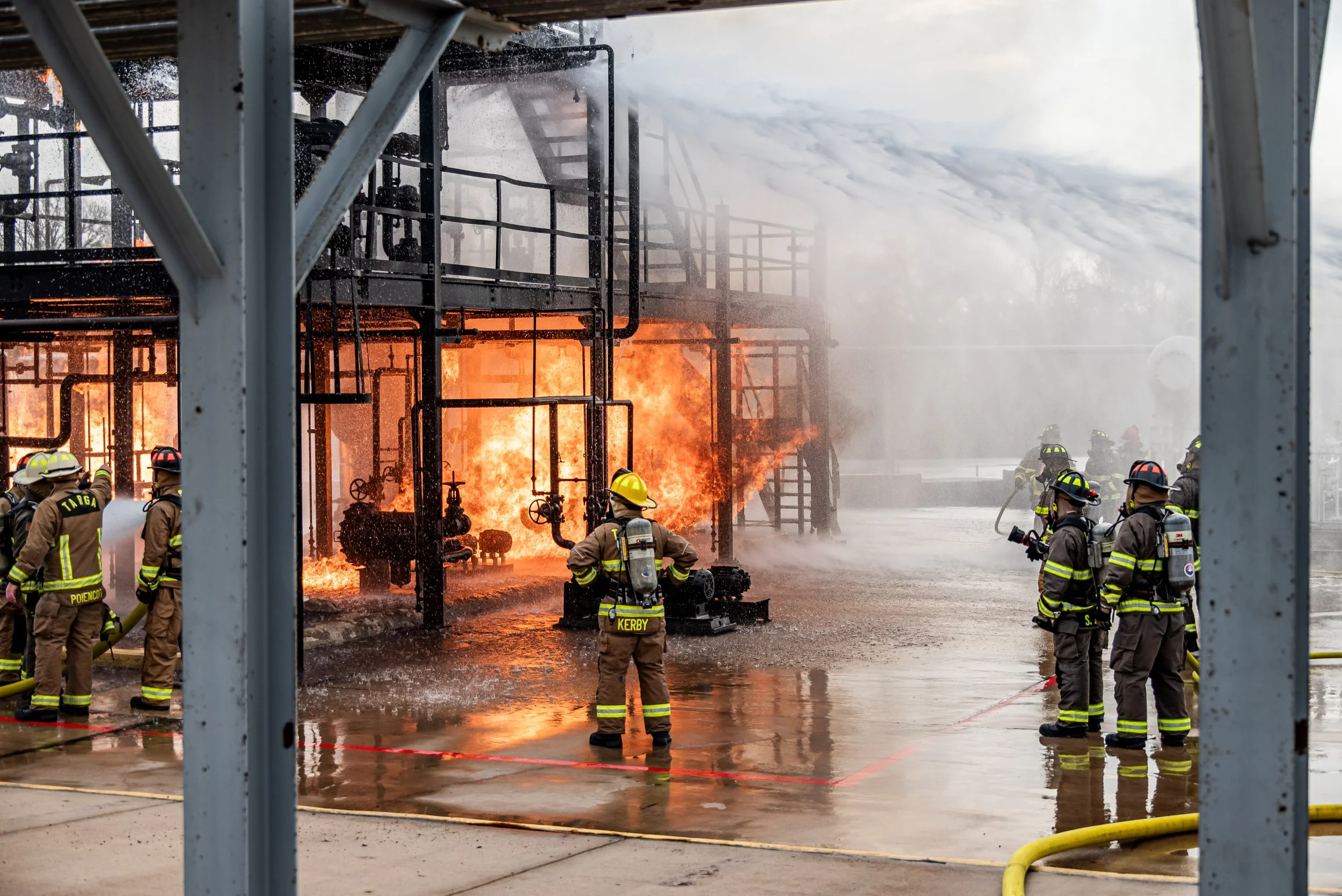 Firefighters putting out a fire at an industrial facility with flames and thick smoke.