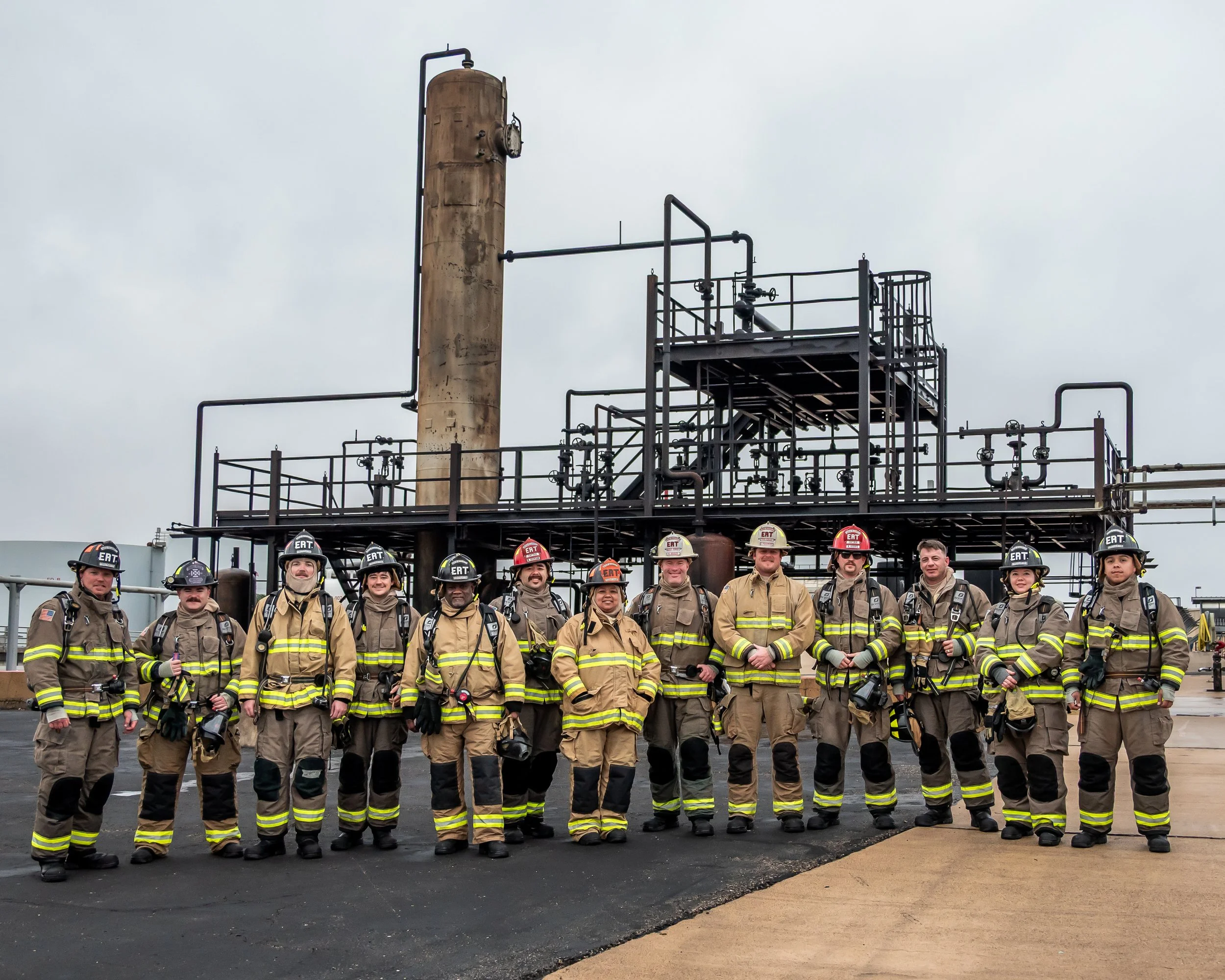 Group of firefighters in uniform standing in front of industrial equipment on a cloudy day.