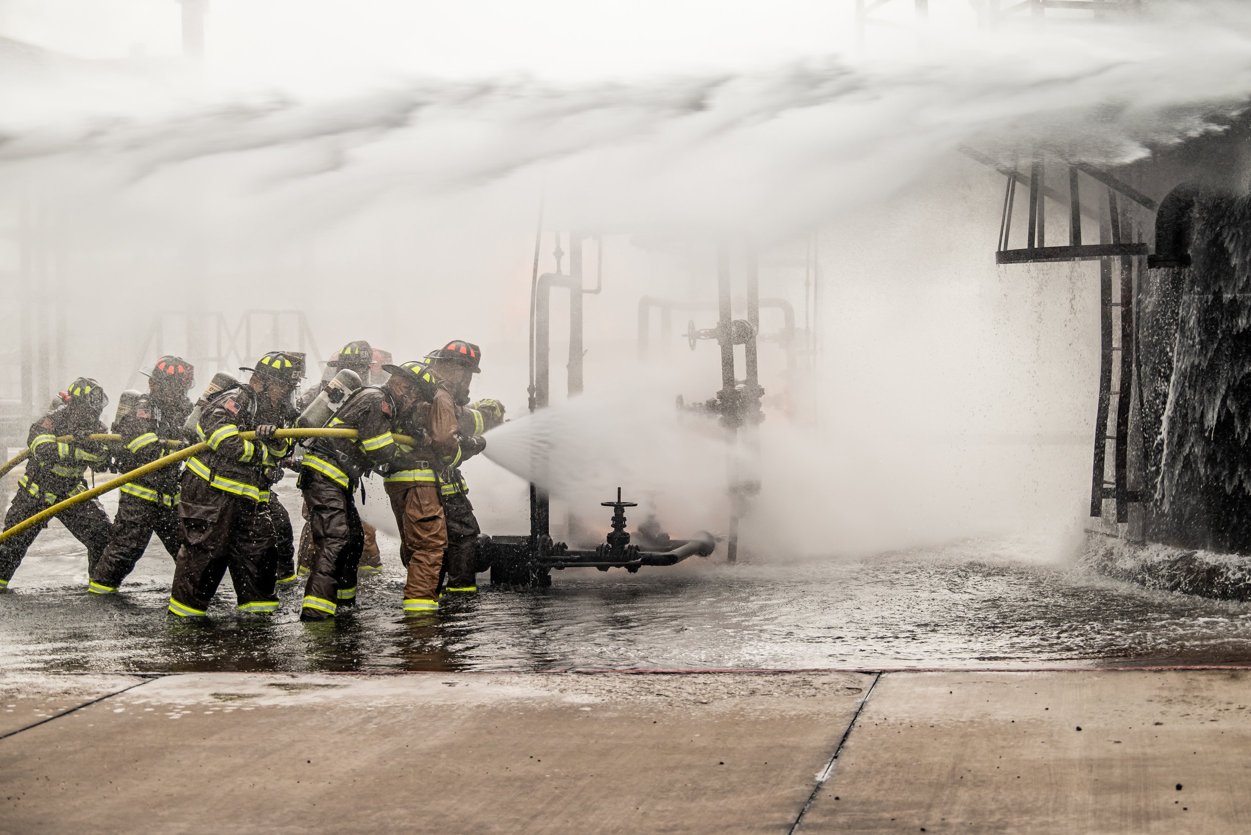 A group of firefighters fighting a fire at a building, spraying water with hoses under heavy spray and thick fog.