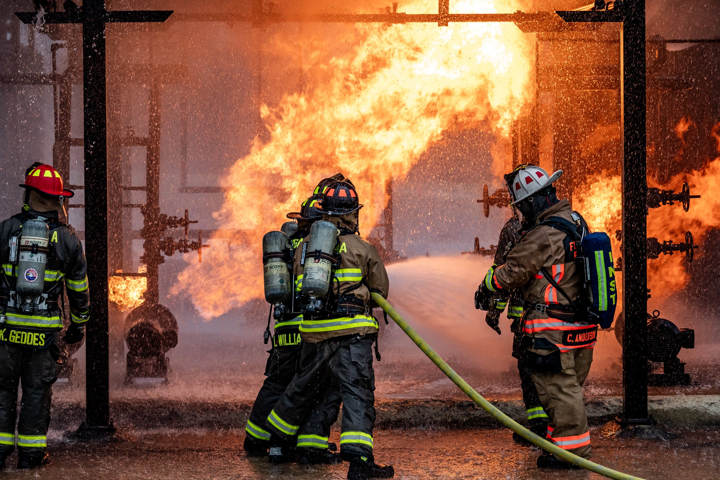 Firefighters in gear battling a large fire, spraying water on the flames with hoses