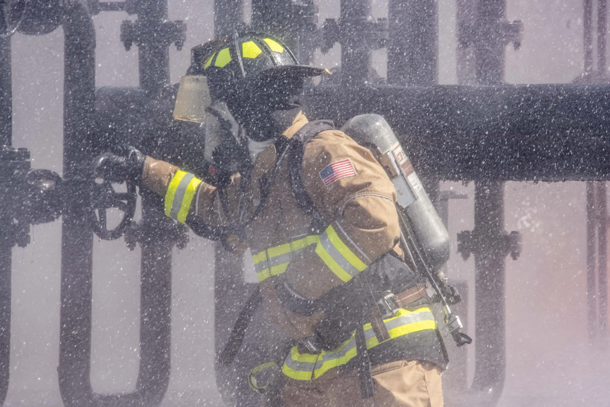 Firefighter in full gear and protective uniform fighting a fire in heavy smoke and ash.