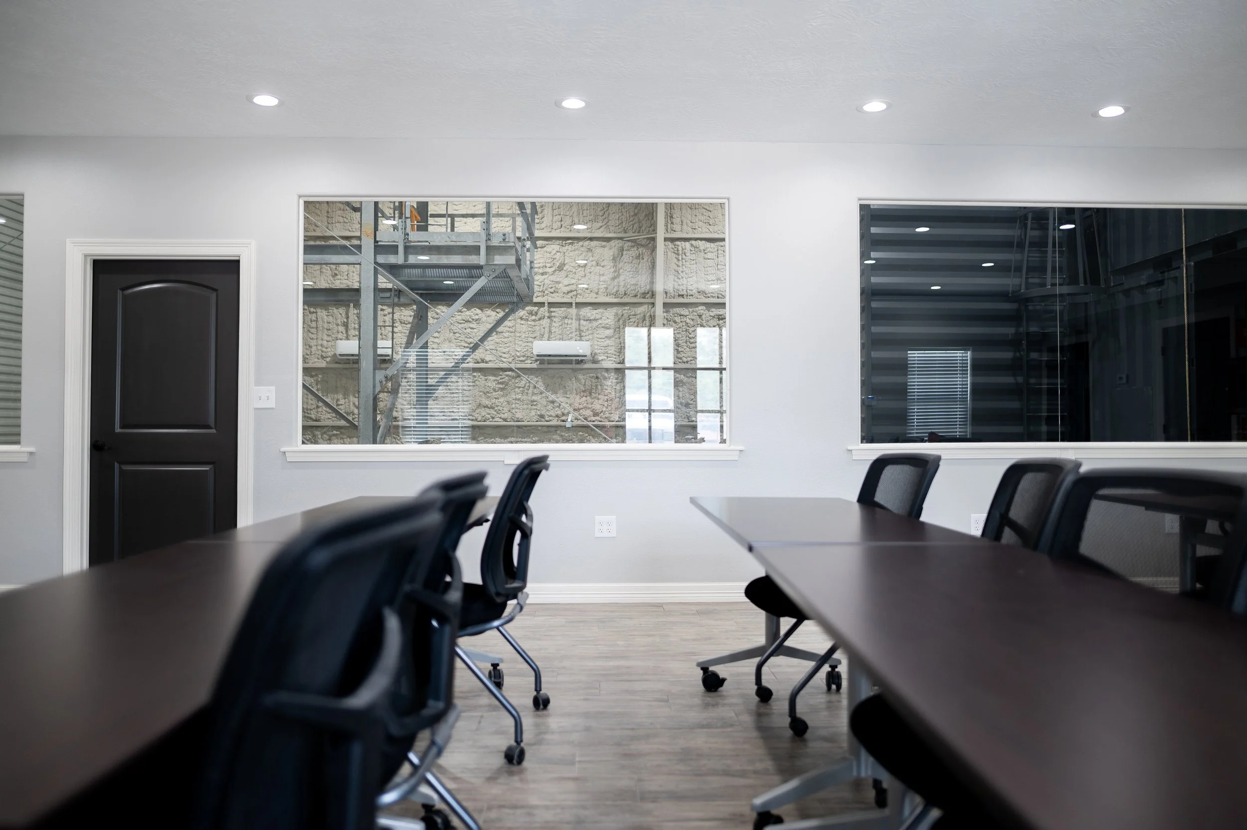 Empty conference room with dark wooden table, black chairs, large windows, and white walls.