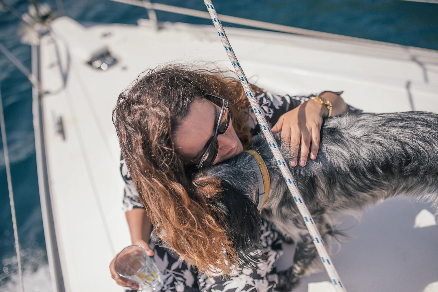 A woman hugging a black and gray dog on a boat, with water in the background.