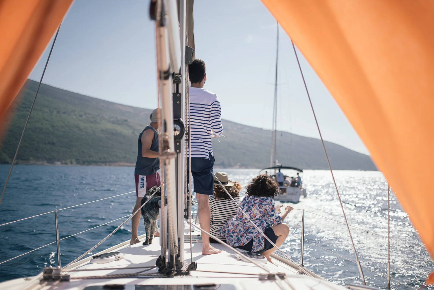 People sitting and standing on a boat, enjoying the water and a boat in the distance, with hills in the background.