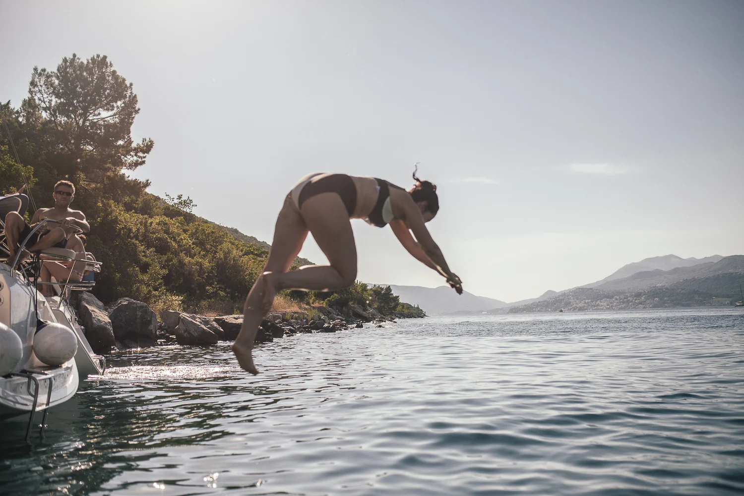A woman diving into a lake from a boat while two people sit on the boat watching.